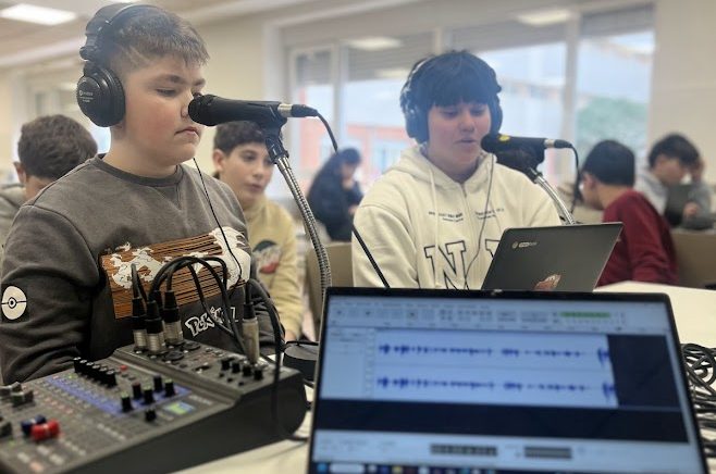 Alumnos de 1º y 2º de la ESO grabando un podcast en clase, con una mesa llena de equipos técnicos como micrófonos, mesa de sonido y ordenadores portátiles, concentrados en la actividad.